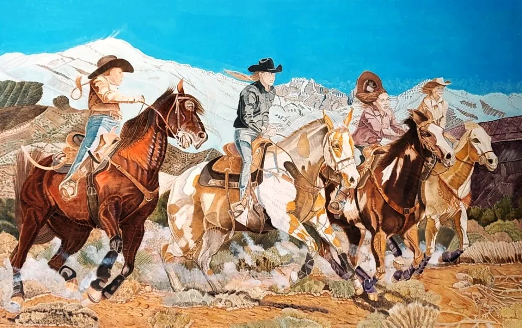 Four female riders racing each other near mountains.